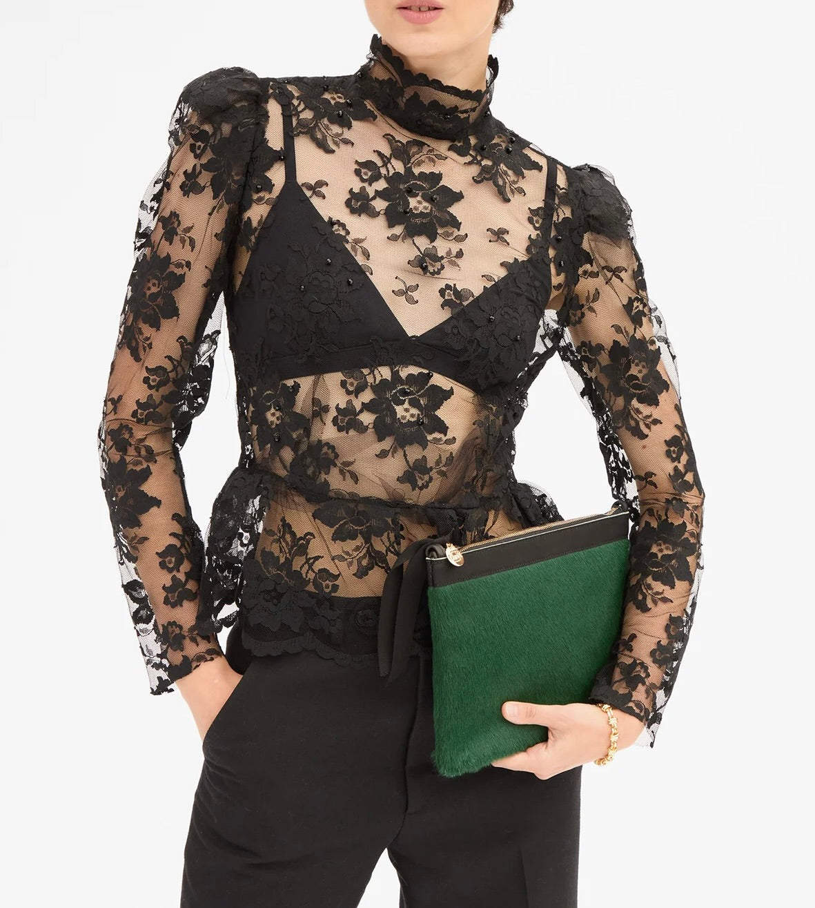 A person holding a Clare V. Flat Clutch Bottle Green, featuring a textured front and black trim.