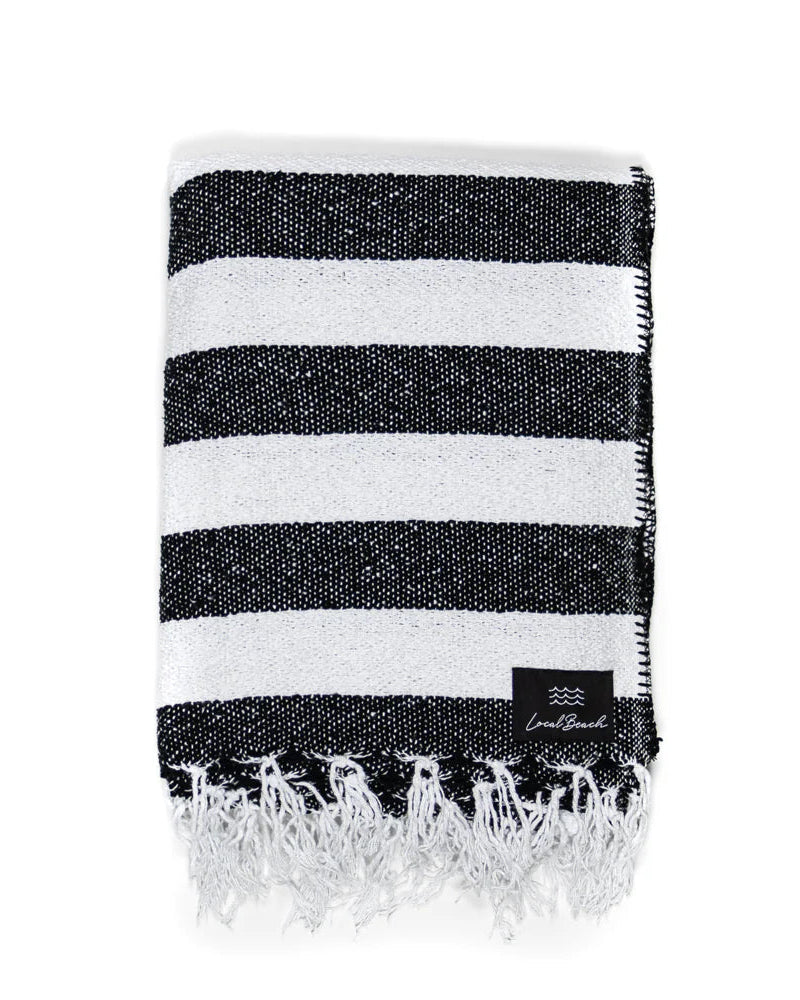 The LOCAL BEACH Baja Beach Blanket is an XL, folded black and white striped throw with fringe ends, a crochet stitch border, and a small black label on one corner.