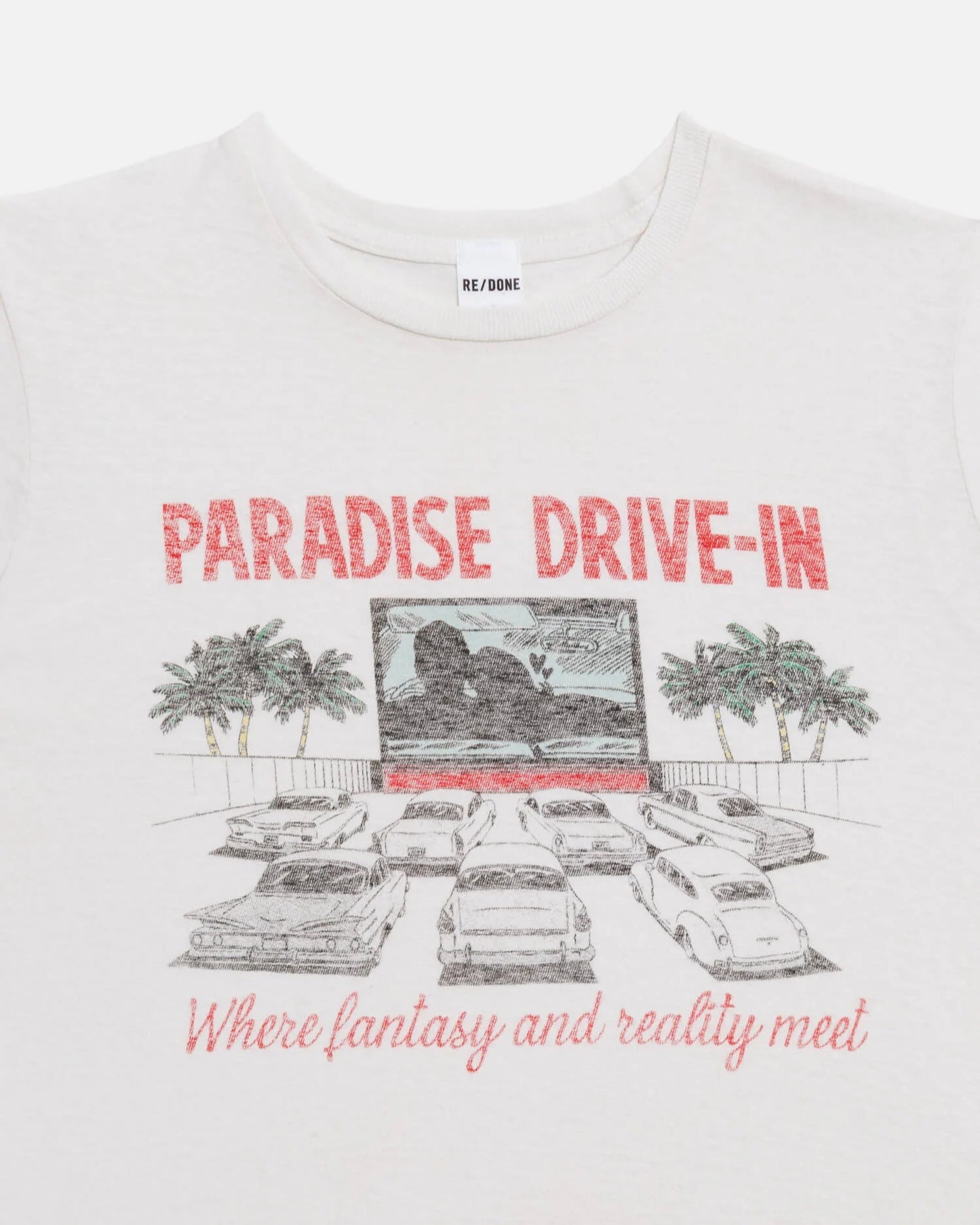 The Drive In Tee by RE/DONE is a white cropped vintage shirt with a drive-in theater graphic—cars, palm trees, and “PARADISE DRIVE-IN” plus “Where fantasy and reality meet.” Inspired by the iconic Paradise Drive In Tee.