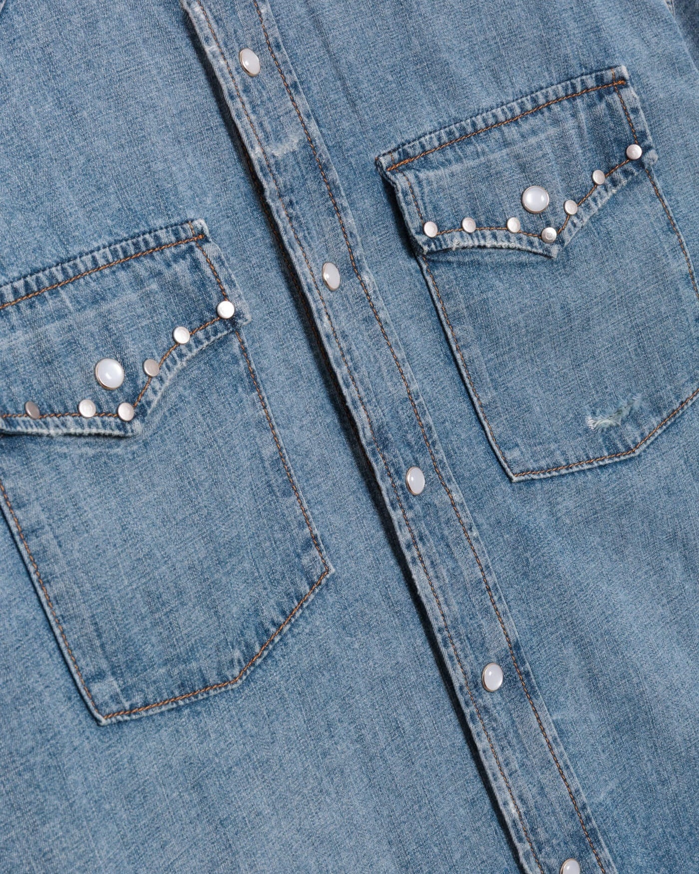 Close-up of a blue denim shirt with studded details on the chest and pocket area.