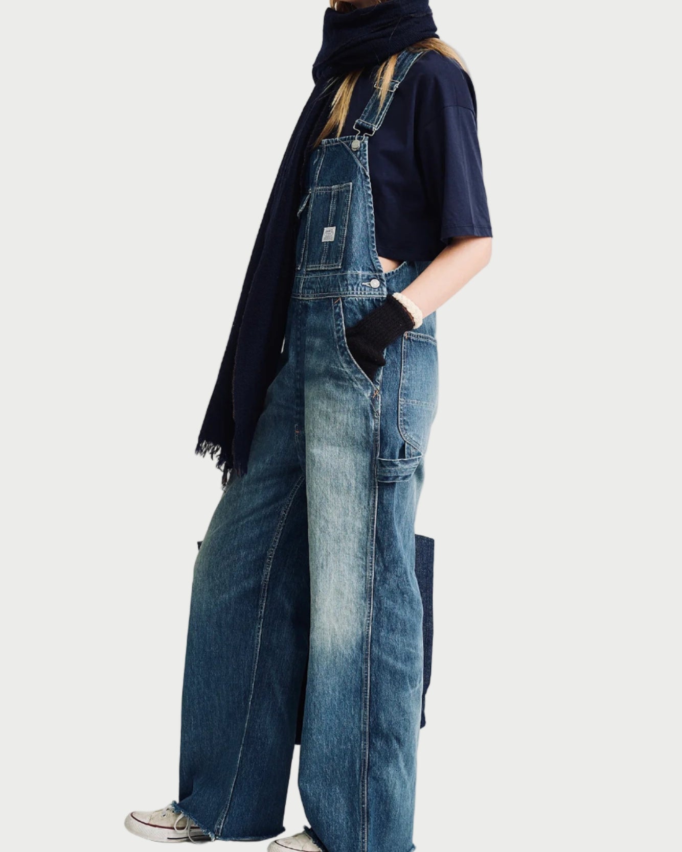 Person wearing denim overalls and a dark jacket on a white background