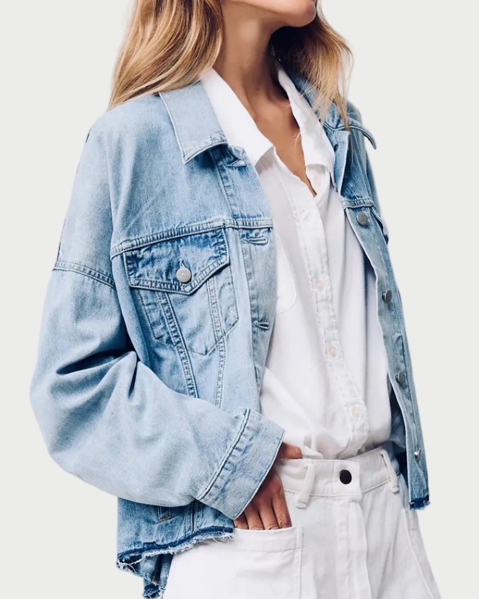 Person wearing a light blue denim jacket over a white shirt and pants on a plain background