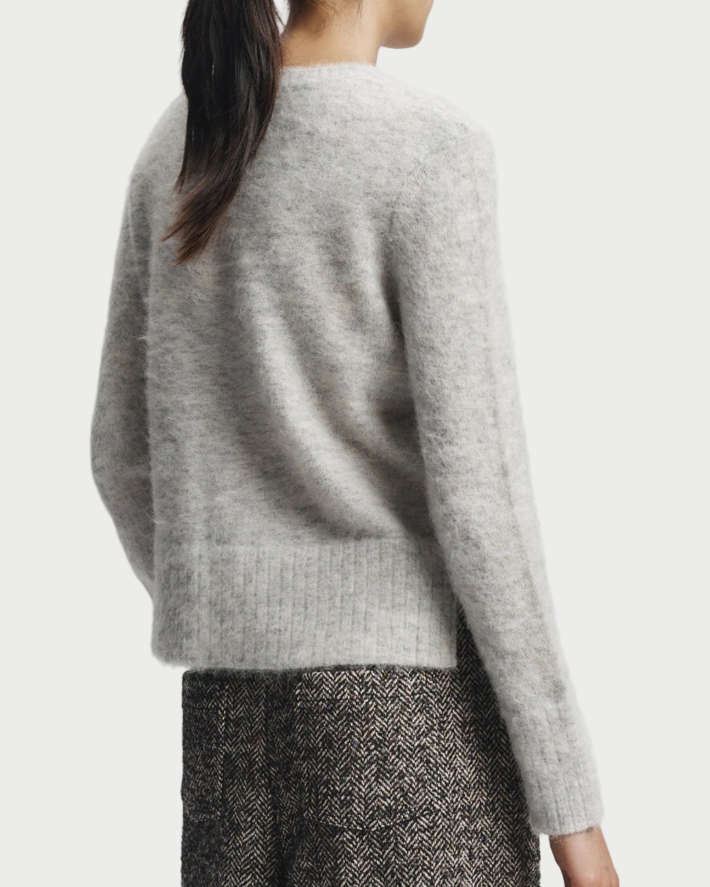 Person wearing a light gray sweater and patterned pants on a white background