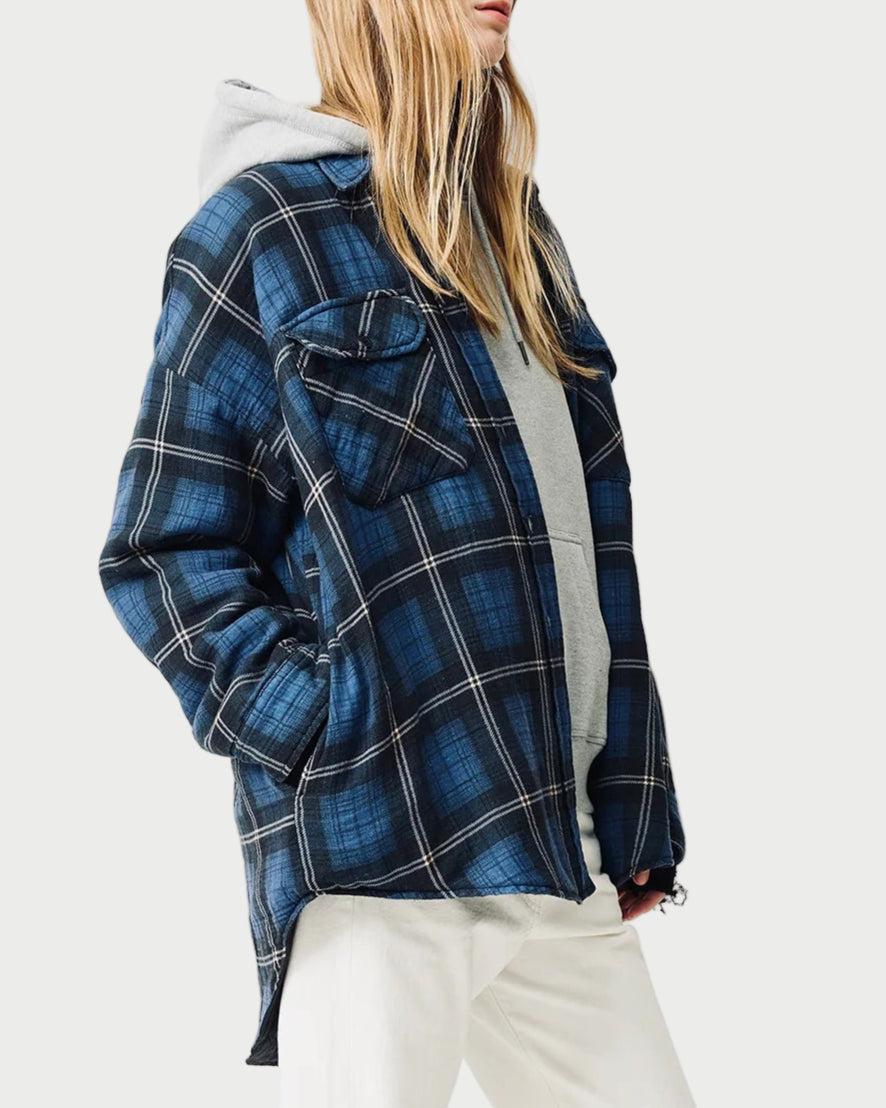 Person wearing a blue plaid jacket over a white hoodie, white pants, and beige sneakers on a white background