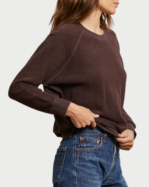 Woman wearing a brown sweater and blue jeans against a plain background