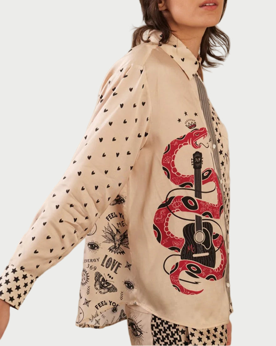 A woman wears the ME369 Scarlett Shirt by ME369—a cream button-down with black heart and star prints, bold red snake wrapped around a black guitar, and unique graphic designs on the front and sleeve.