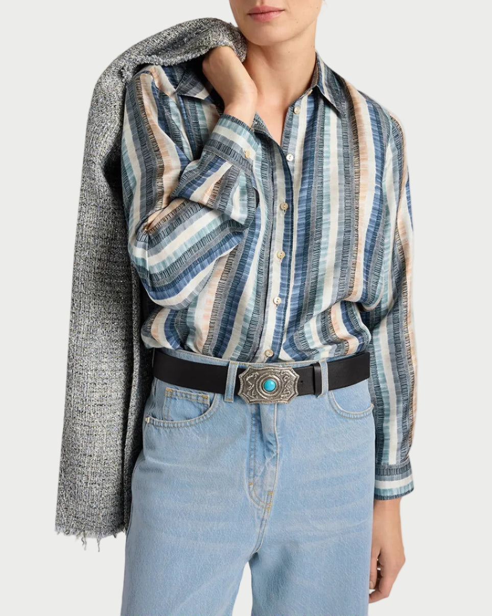 A person wears the Momoni Arles Shirt by Momoni with light blue jeans, a black belt featuring an ornate buckle, and holds a textured gray jacket over their shoulder. Their face is partially out of frame.