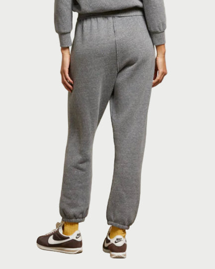 Person wearing a gray sweater and pants set against a plain wall.
