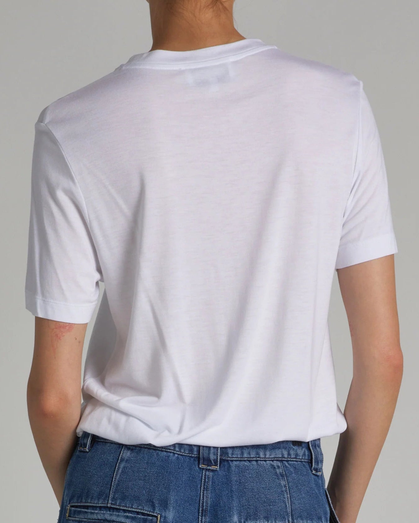 Person wearing a plain white t-shirt and blue jeans against a neutral background