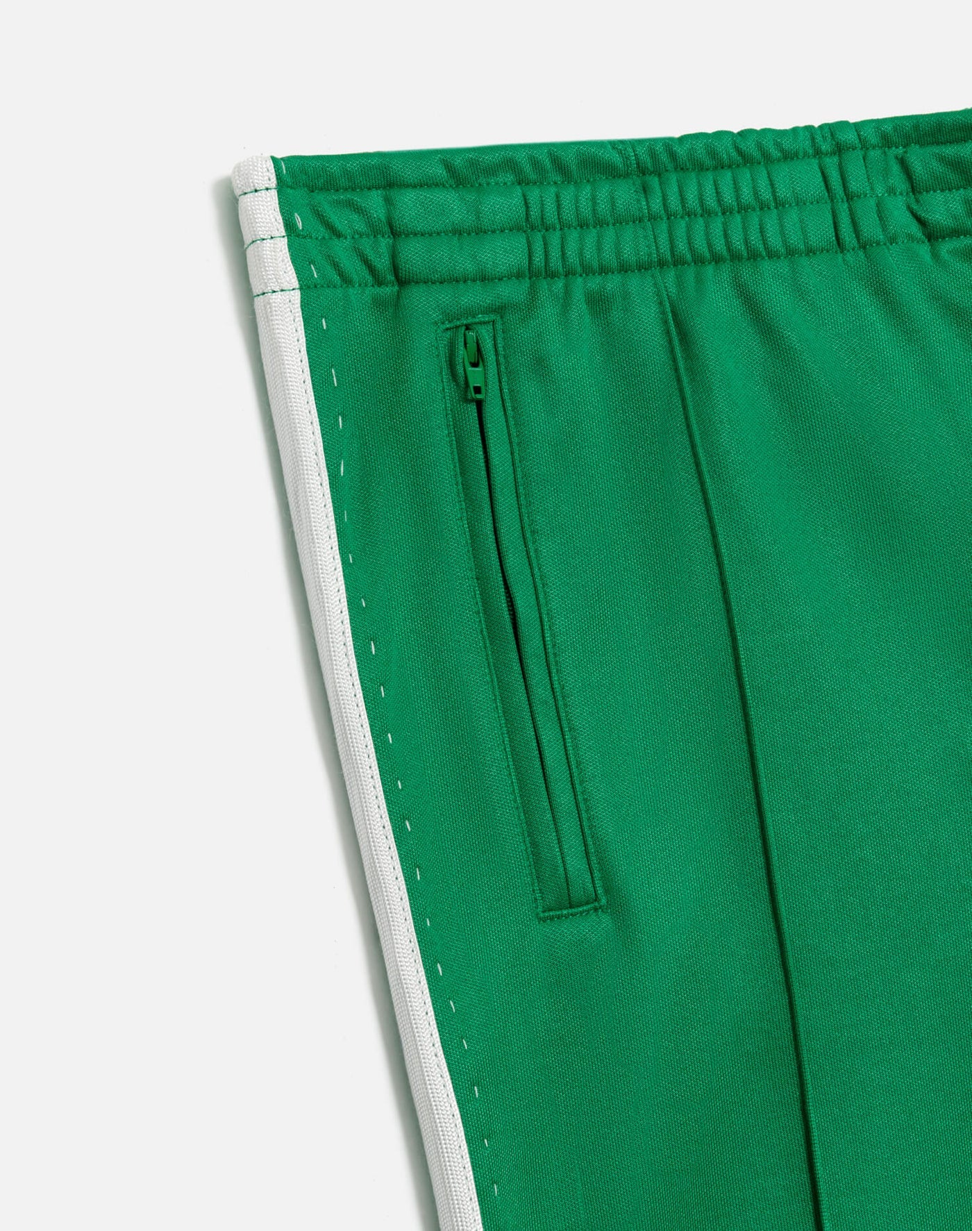 Close-up of RE/DONE’s Sunland Track Pant in green, featuring an elastic waistband, zippered side pocket, and white side stripe. Smooth fabric offers a sleek, sporty look with modern Western-inspired style.