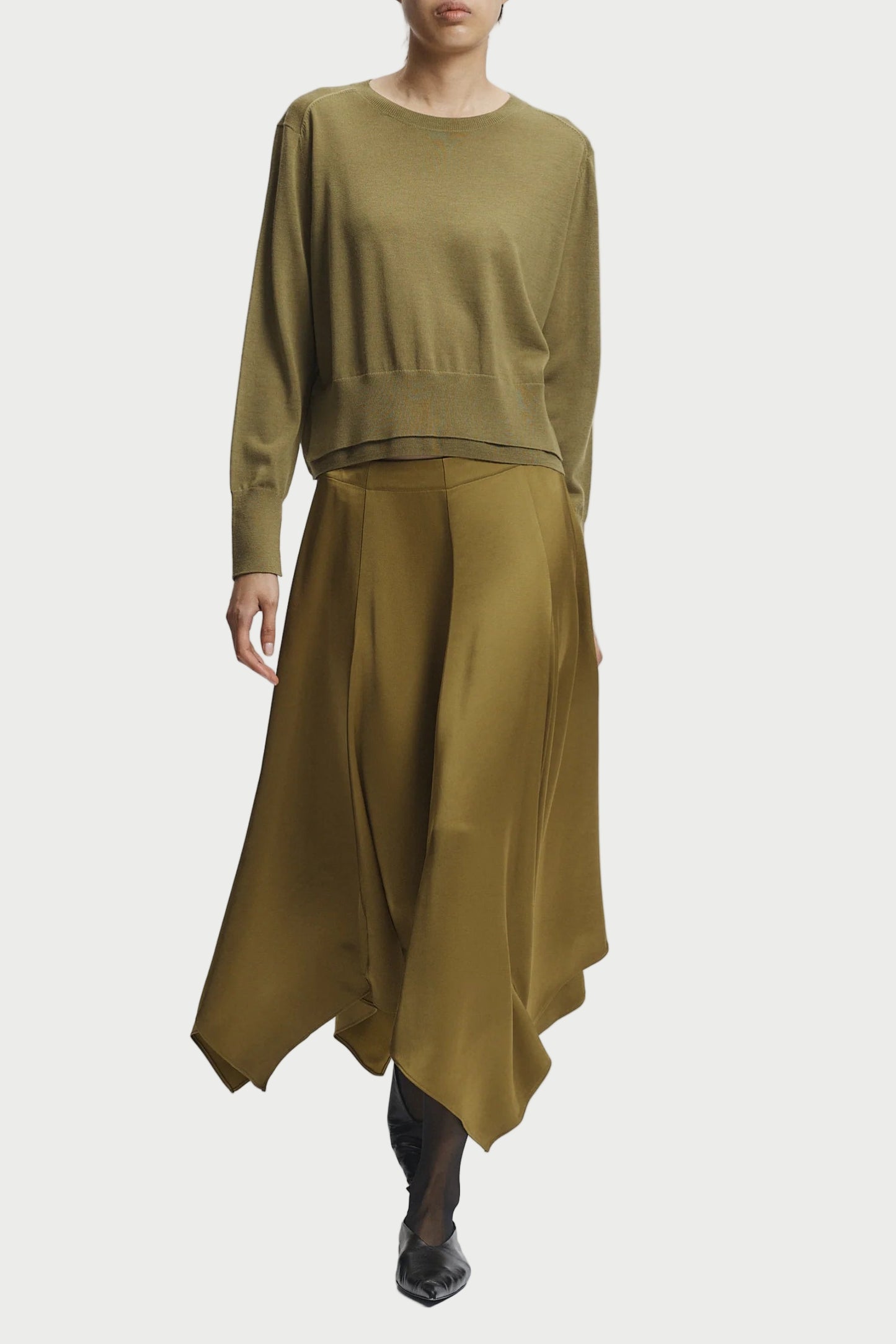 Person wearing a green outfit with a top and long skirt on a white background