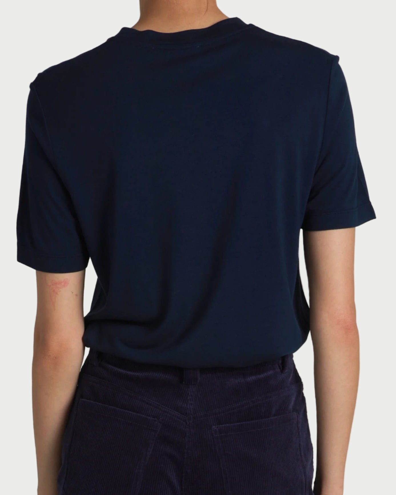 A person is seen from the back wearing the Saint Art Zola Crewneck Navy Tee by Saint Art NY with dark pants against a plain, light-colored background.