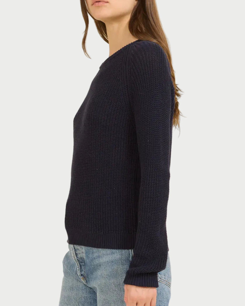 Woman wearing a navy sweater and light blue jeans on a beige background