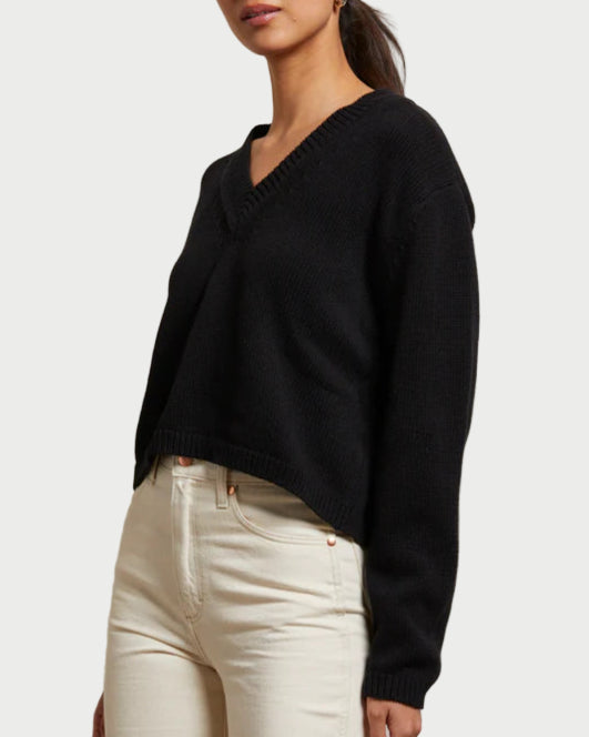 Woman wearing a black sweater and white pants against a plain background