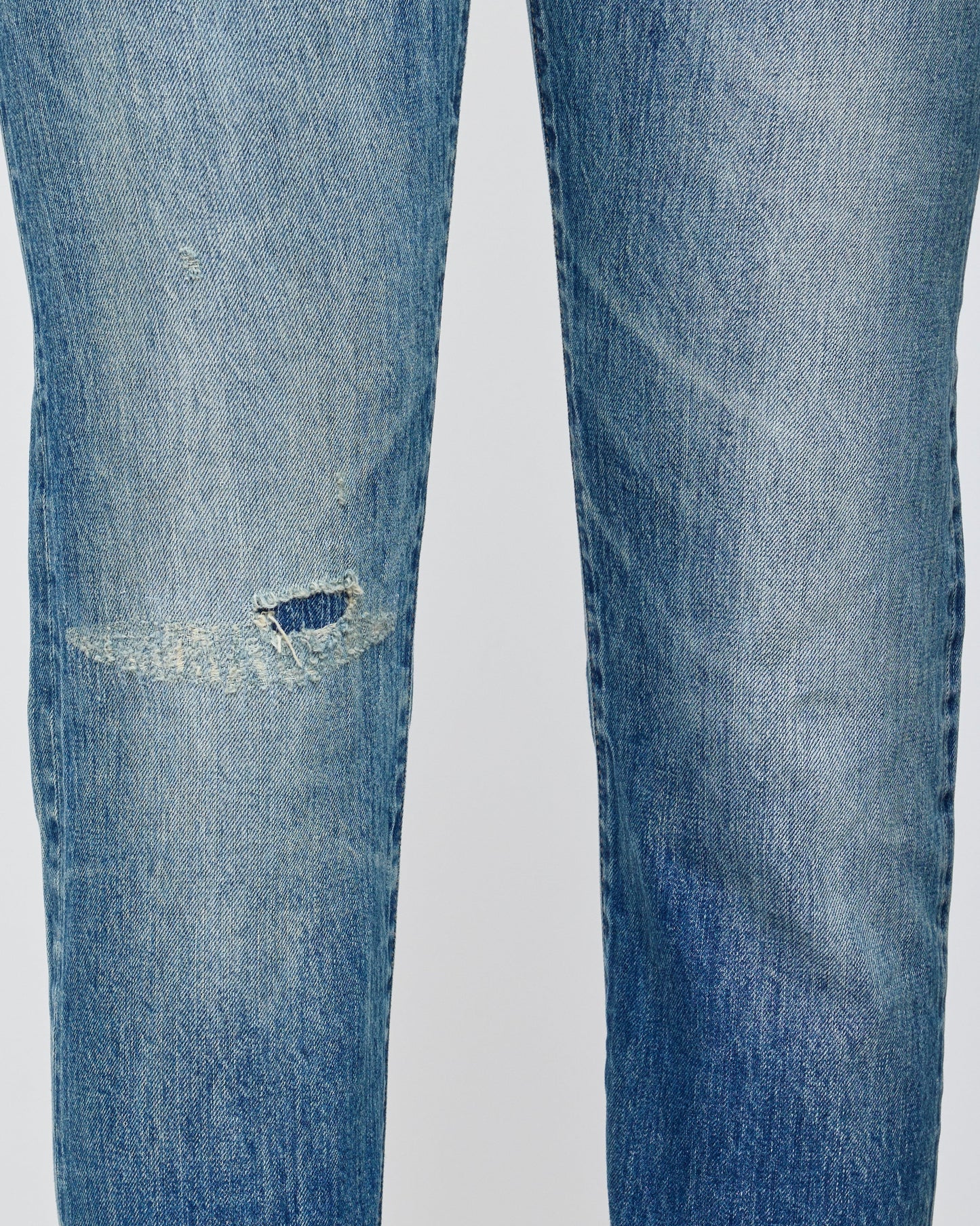 Close-up of blue jeans with a tear on a light gray background