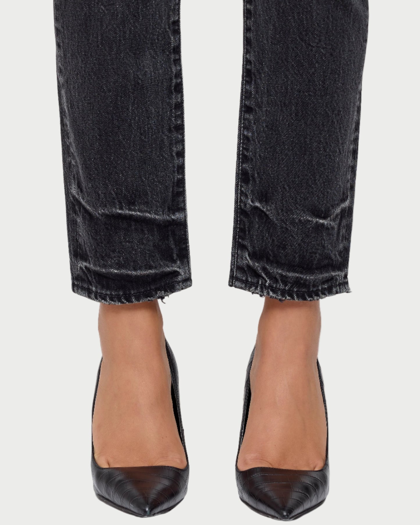 Black high-heeled shoes worn with black jeans on a white background