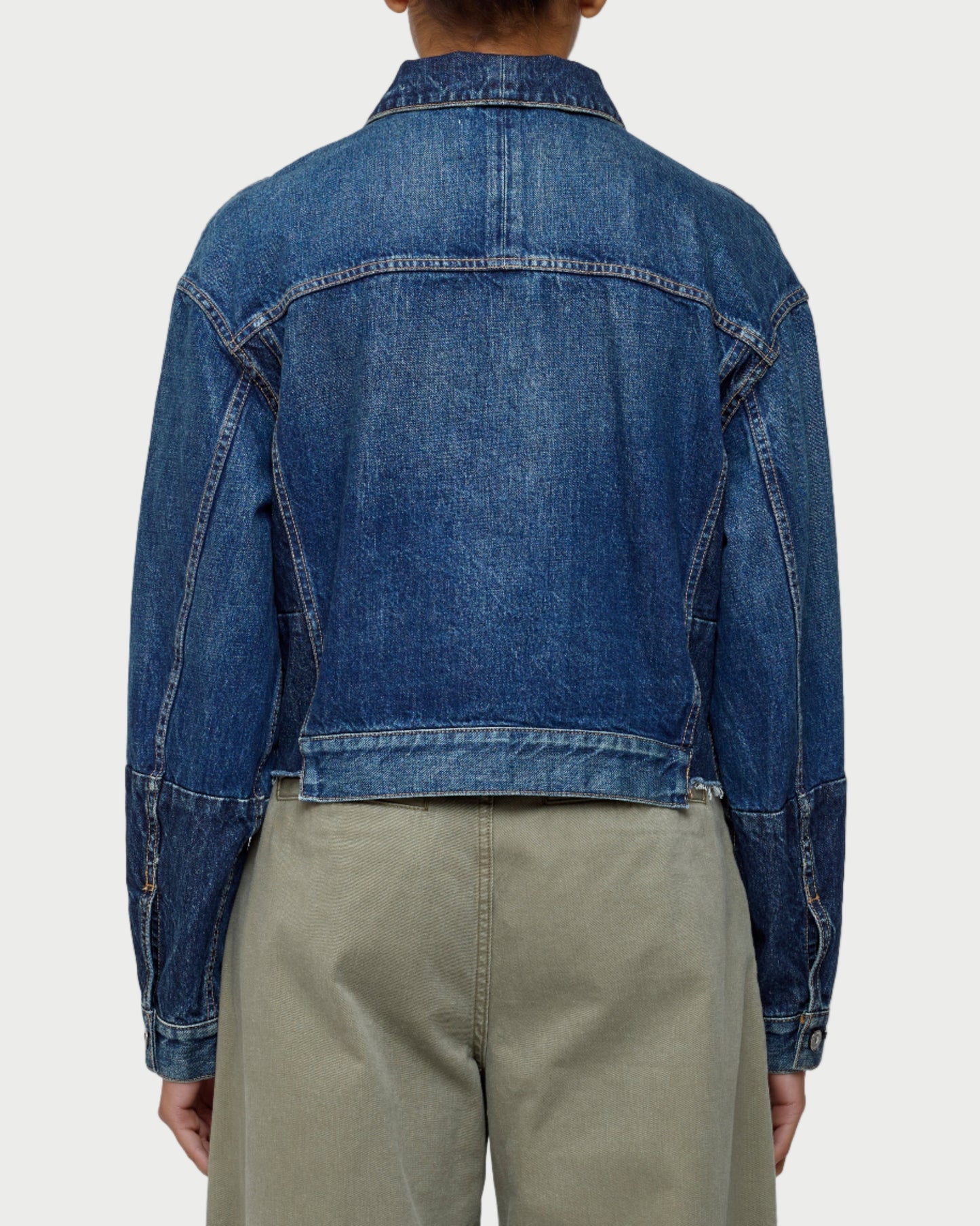 Person wearing a blue denim jacket and beige pants on a white background