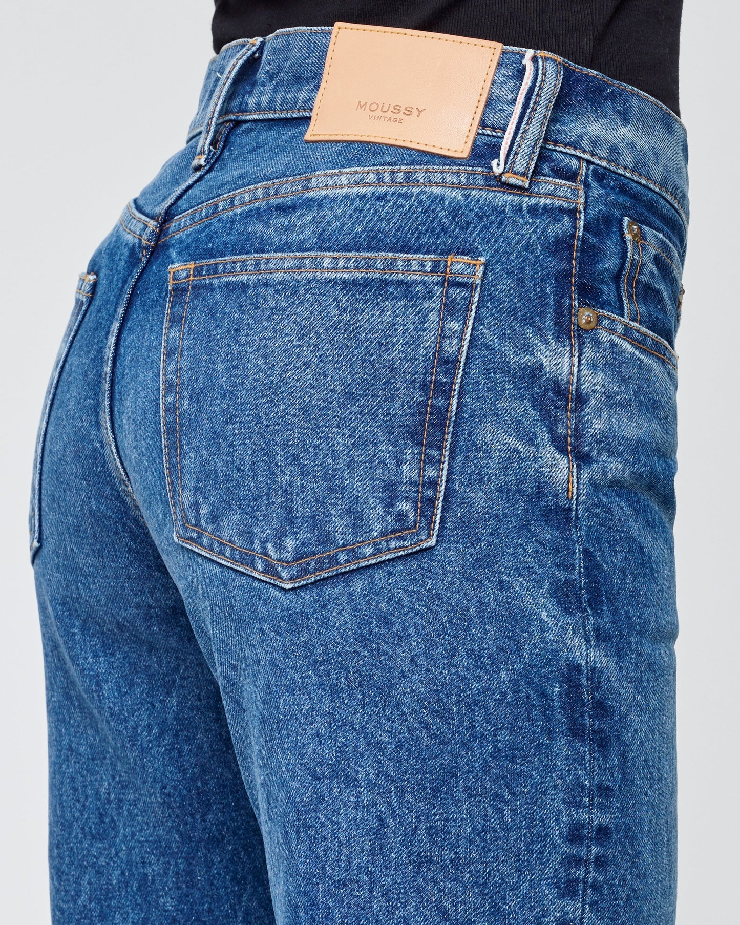 Blue jeans with a brand label on the back pocket against a light gray background