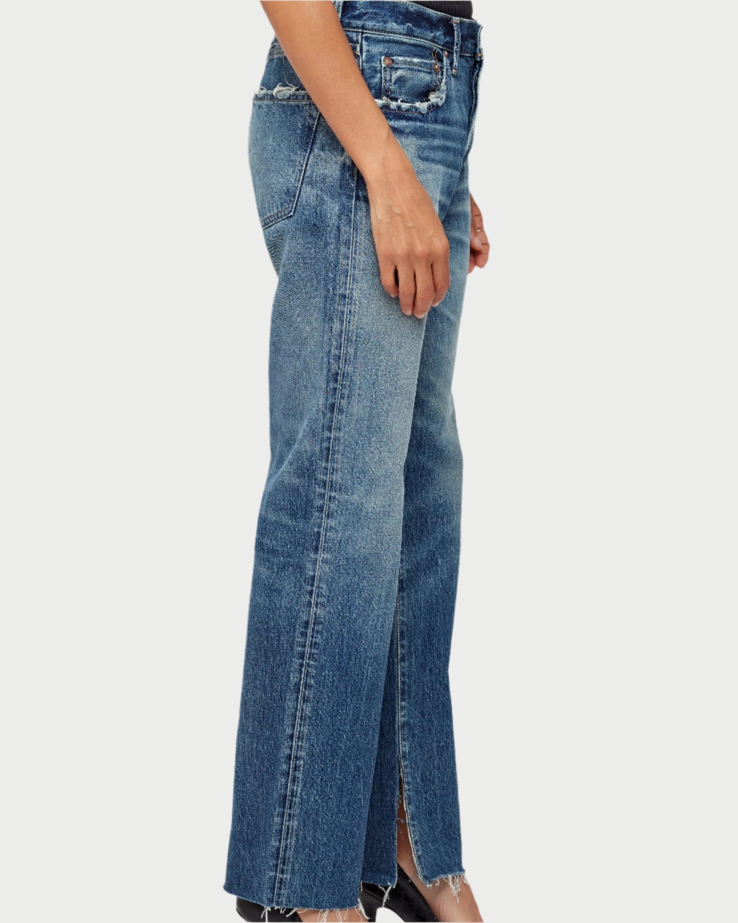 Blue jeans with a front slit worn by a person on a light gray background