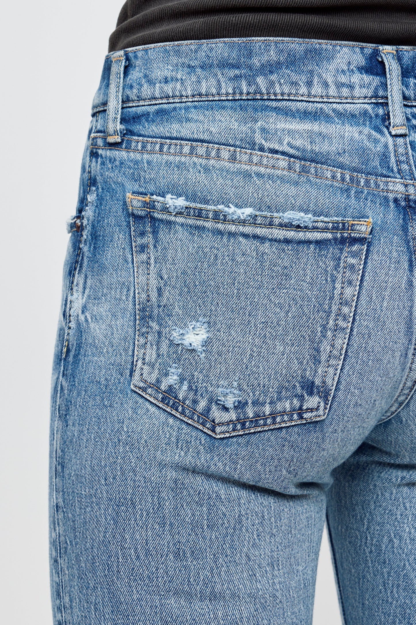 Close-up of the back of a person wearing Moussy Farmingdale Slim Straight Jeans in light blue with distressed details and frayed back pocket, styled with a black top.