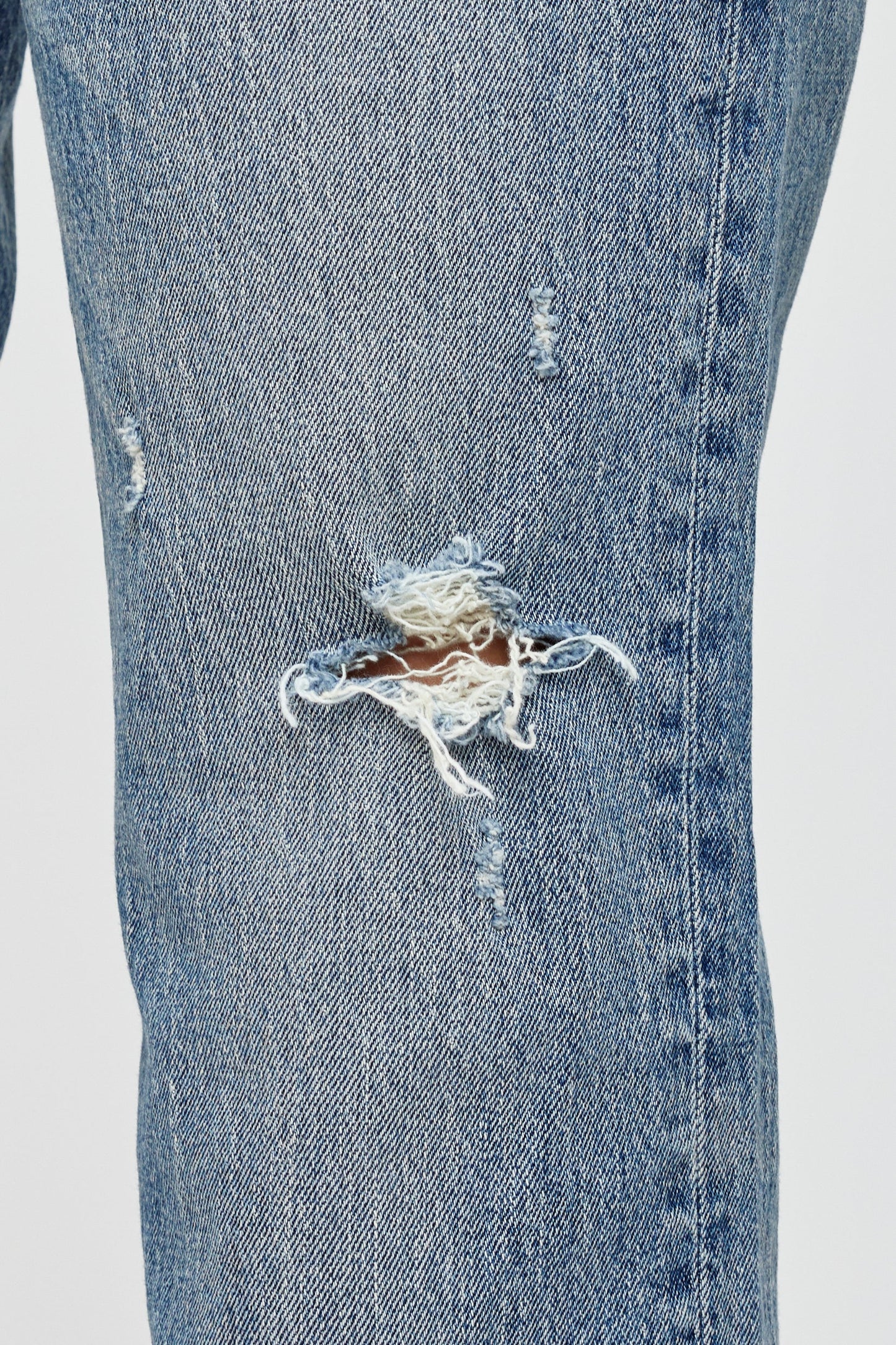 Close-up of the Moussy Massapequa Straight Leg Jeans, featuring a large frayed hole on the thigh and smaller distressed patches that reveal white threads and some skin beneath.
