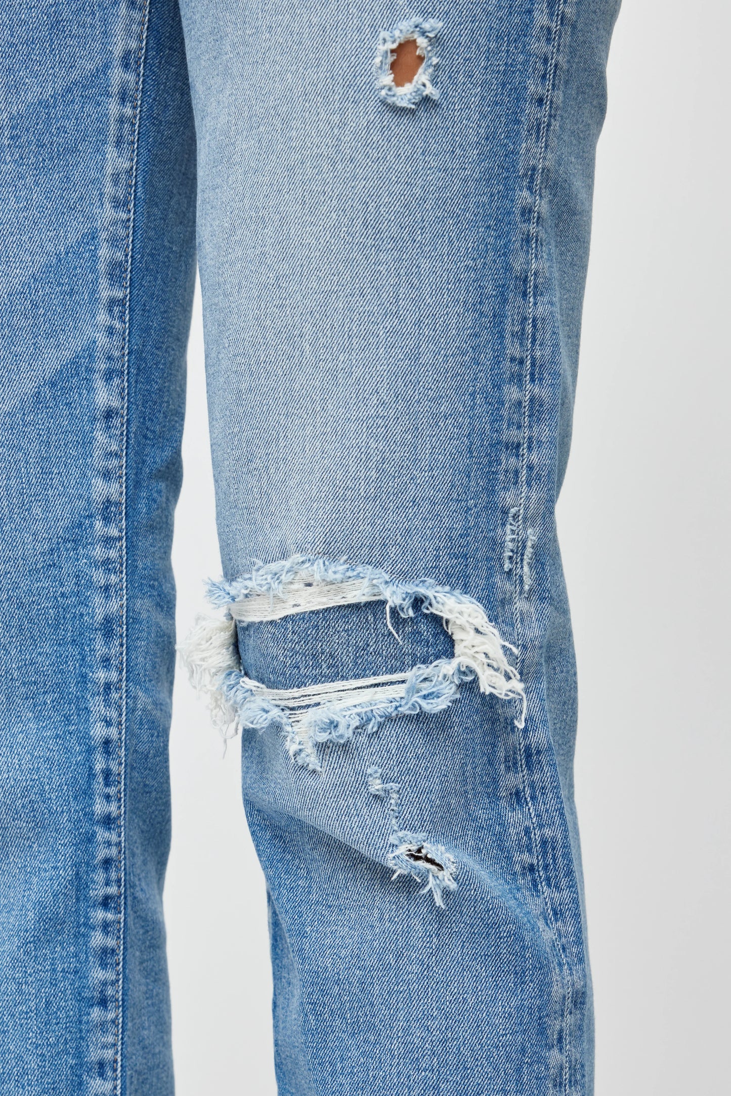 Close-up of a pair of blue jeans with multiple tears on a white background