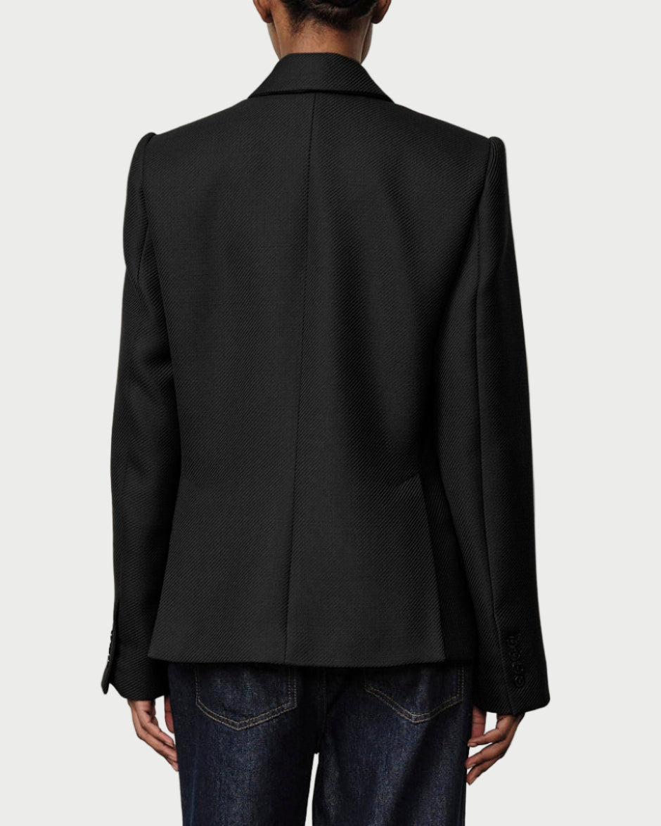 Person wearing a black suit standing against a plain white wall.