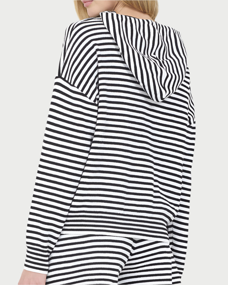 A person wears the One Grey Day Stripe Warwick Hoodie—a black and white cotton-blend hoodie with bold horizontal stripes and matching pants—shown from the back with the hood up, creating a modern, lightweight look.