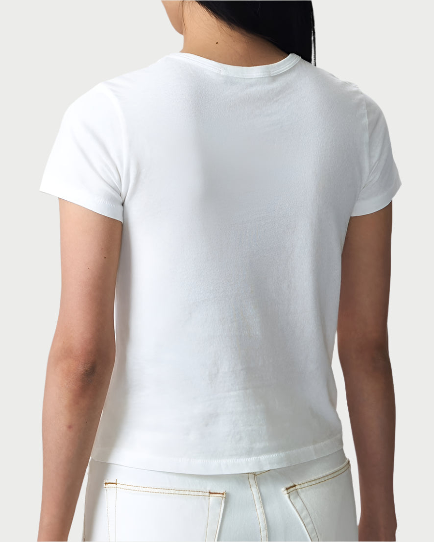 A person in a vintage style, wearing the SLVRLAKE Baby Tee and white pants, stands with their back to viewers against a light gray background. This 100% cotton outfit by SLVRLAKE exudes timeless style and comfort.