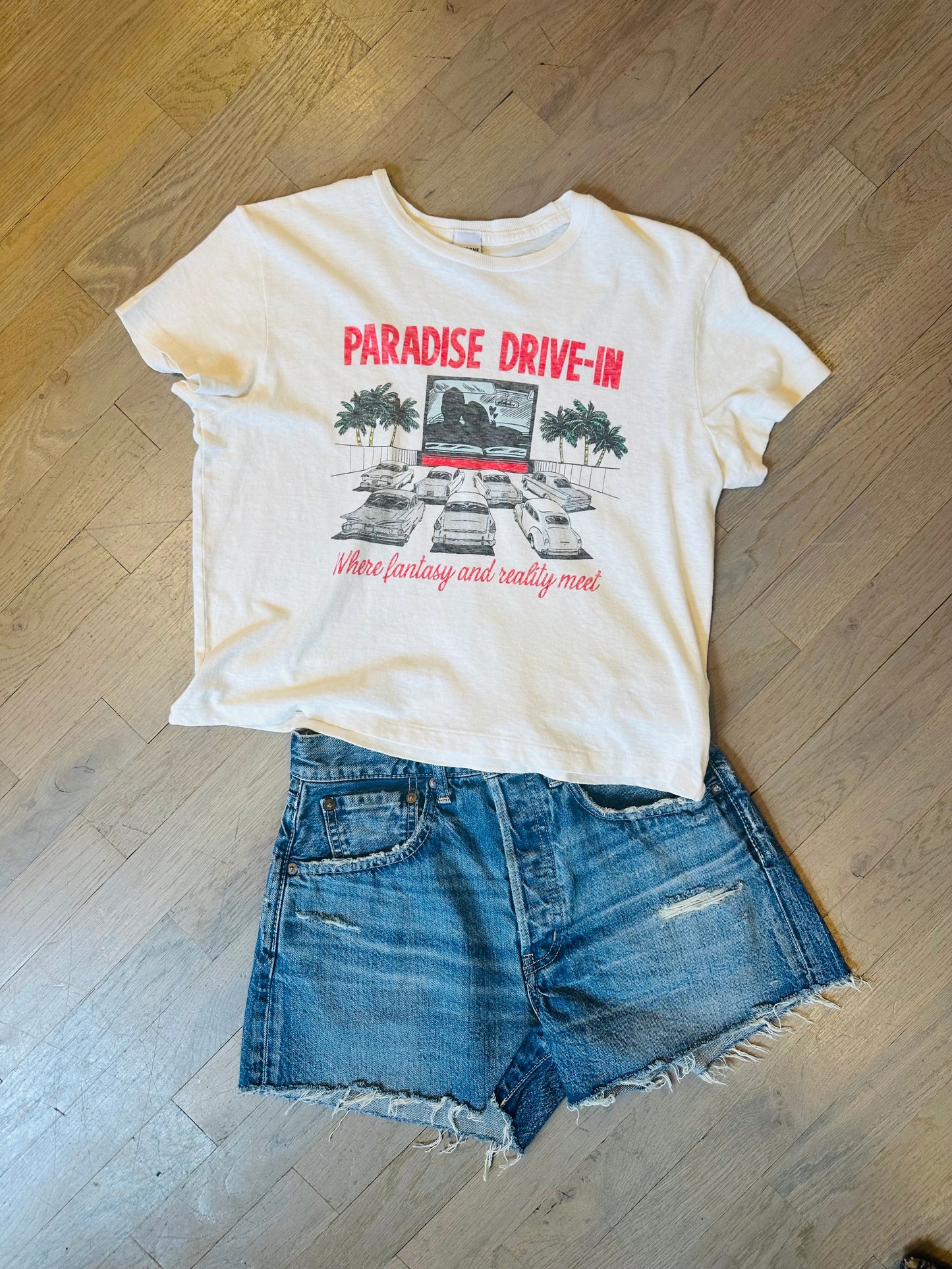 A RE/DONE Drive In Tee and denim cutoff shorts are laid flat on a wooden floor.