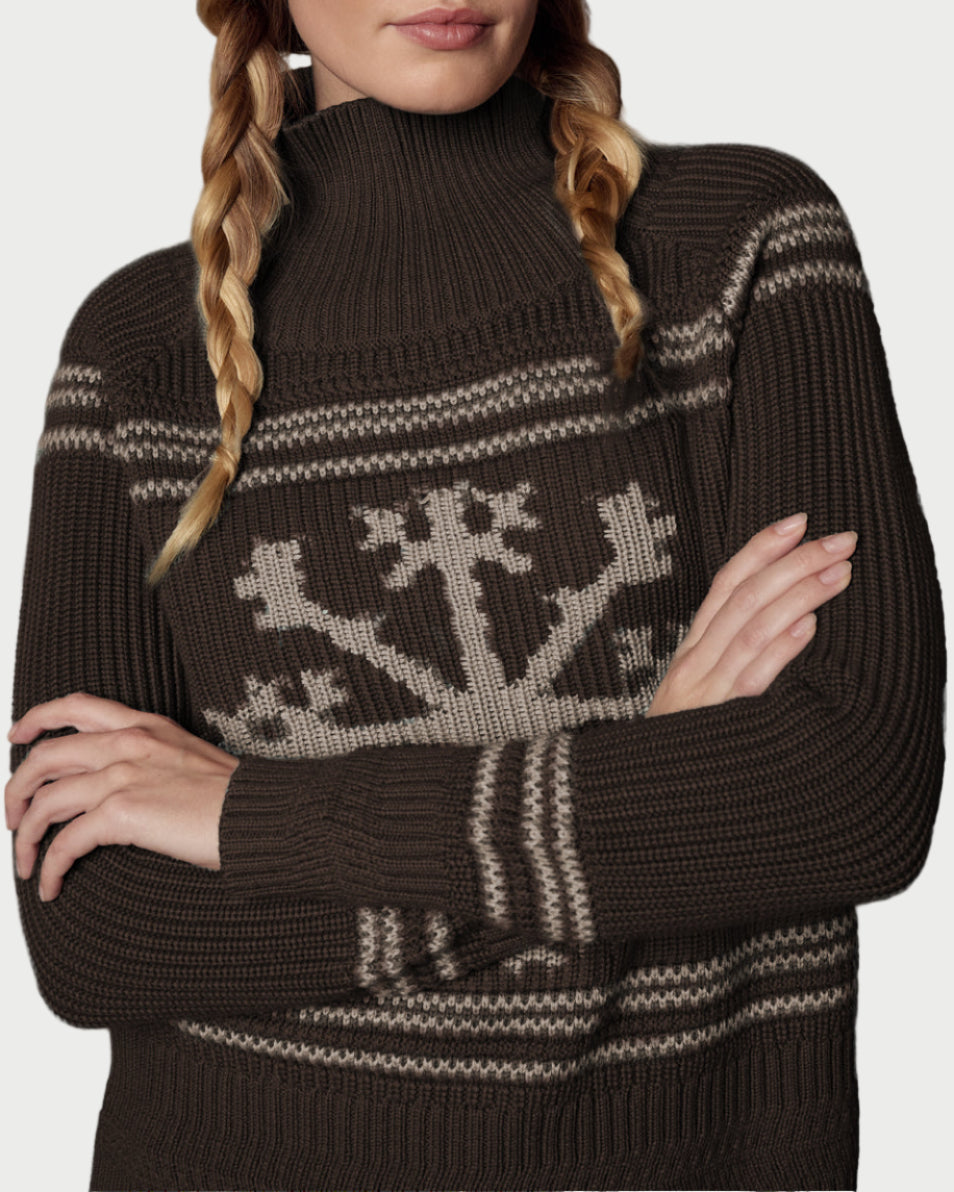 Woman wearing a brown knit sweater with a pattern and matching beanie with 'APRES' text against a textured gray background.