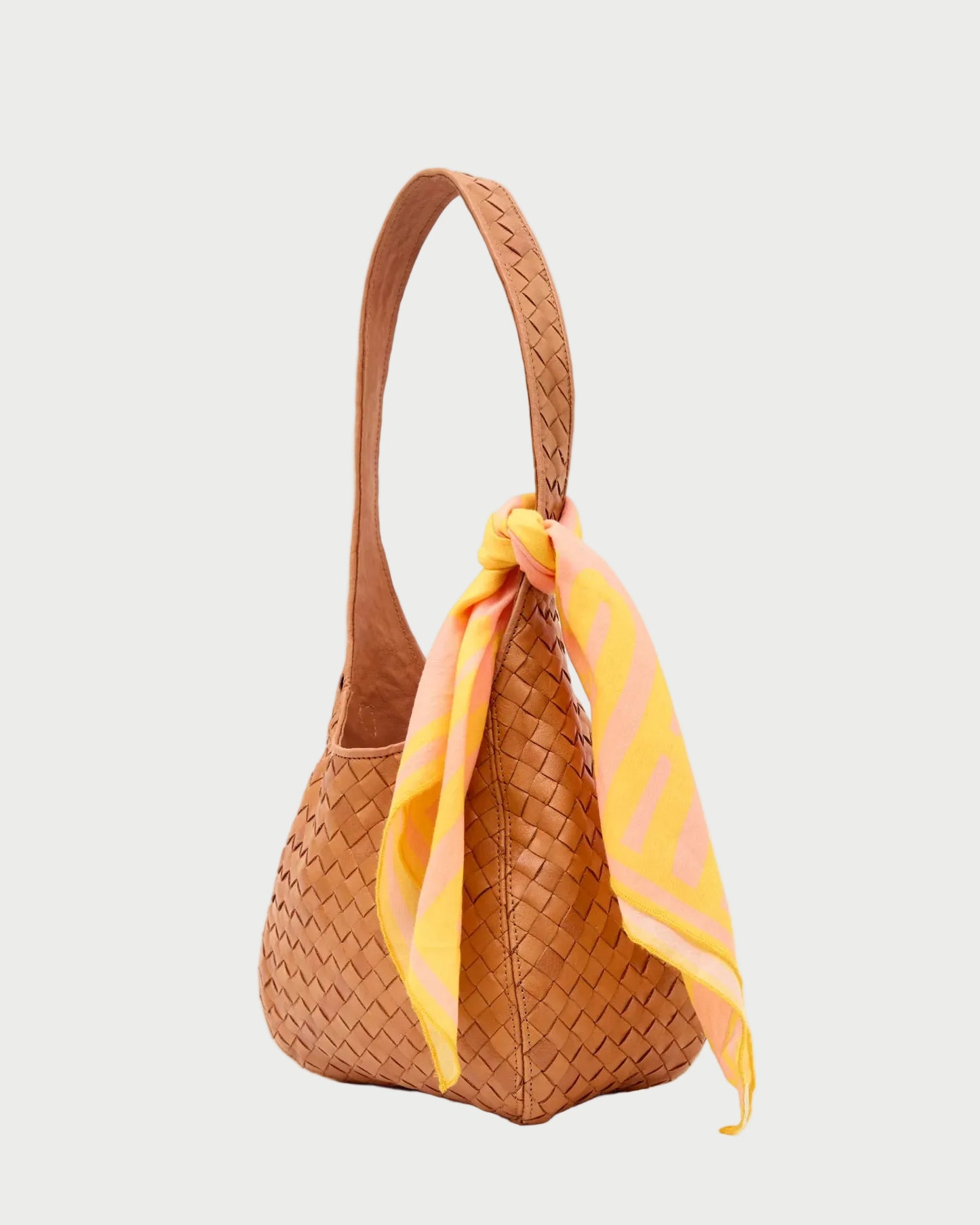 Brown woven handbag with a yellow and pink scarf draped over it on a white background
