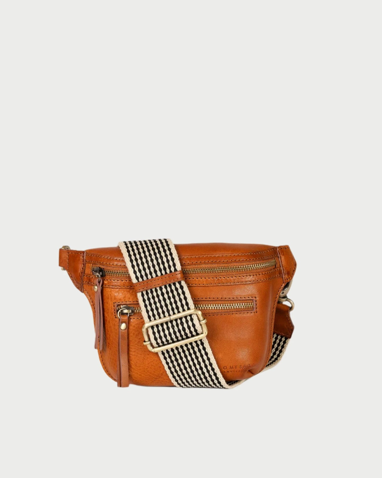 Introducing the Beck's Bum Bag in Cognac by O MY BAG, a stylish brown leather crossbody with a striped adjustable strap. This sleek design merges practicality and fashion, featuring two zippered compartments for convenience.