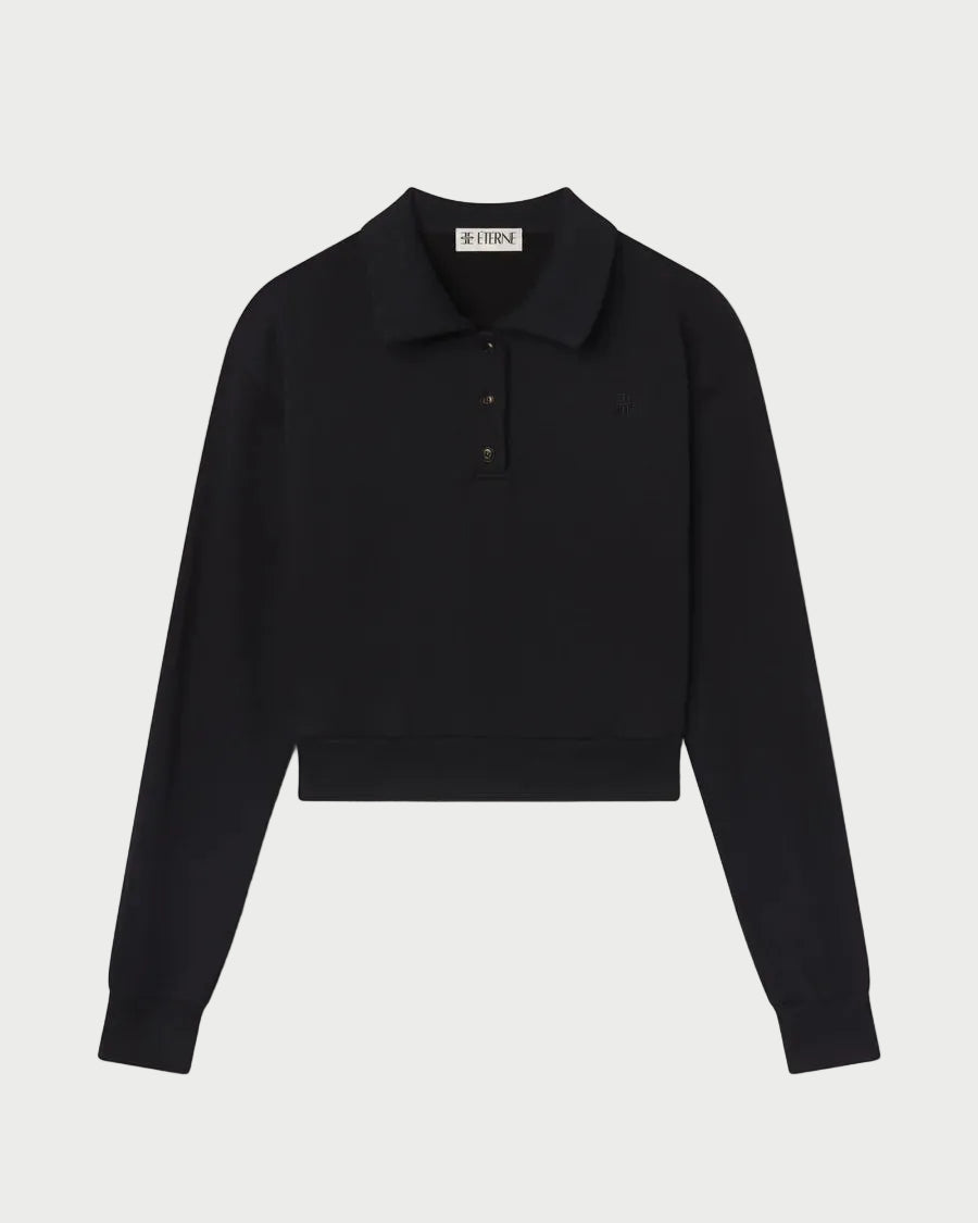 The Éterne Cropped Polo Sweatshirt by Eterne is a black, long-sleeve cropped sweatshirt featuring a collar and three buttons at the top. Crafted from soft French terry for a relaxed fit, it is displayed on a white background.