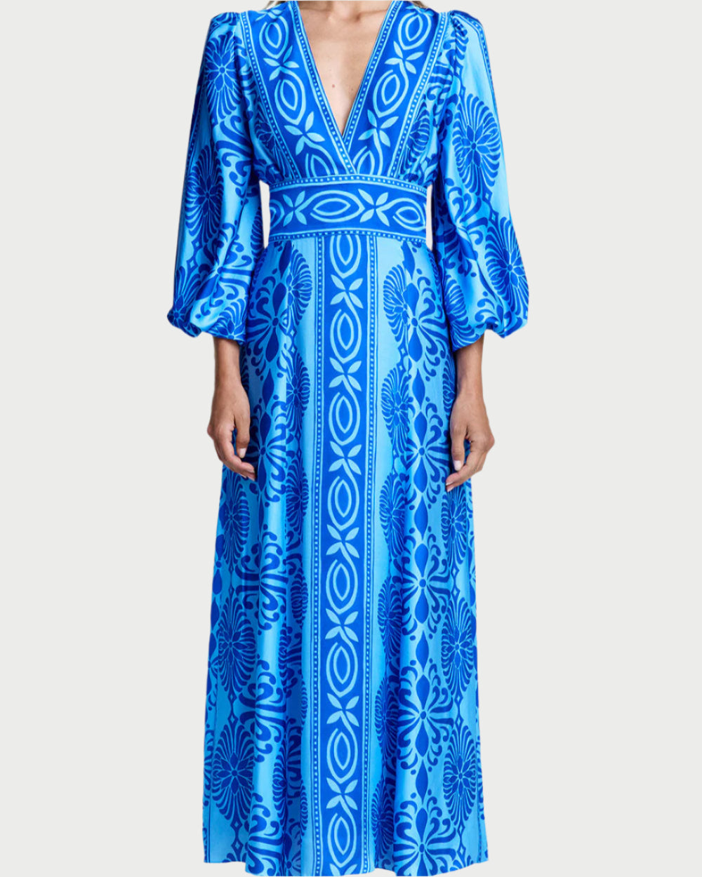 A person is wearing Smythe's stunning Crossover Midi Dress, featuring bold geometric and floral patterns in a multi-blue hue. The outfit boasts sophisticated puffed lantern sleeves and a deep V-neckline, creating an effortlessly chic look.