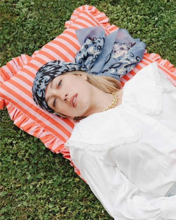 Person lying on a striped mat with a headscarf in a grassy area