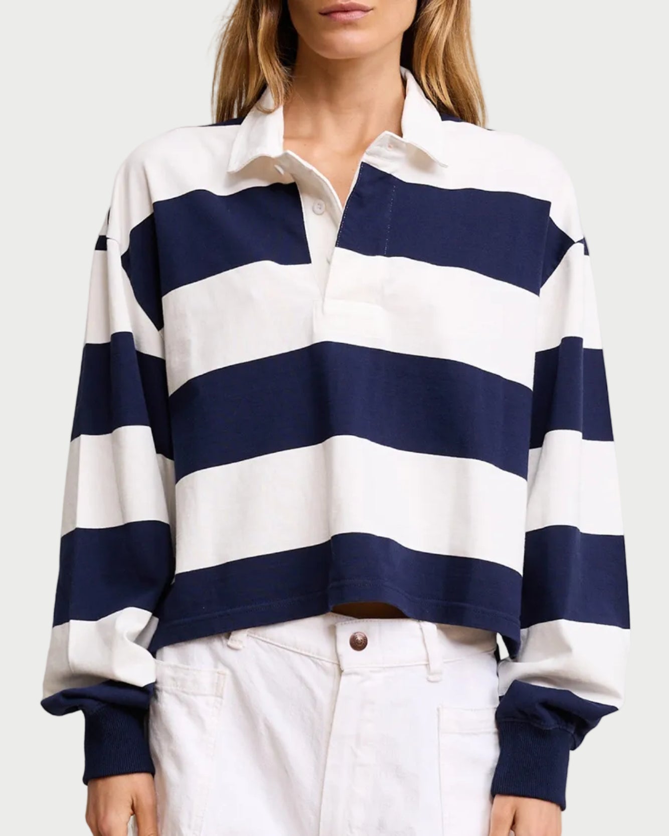 Person wearing a navy and white striped shirt with white pants on a plain background