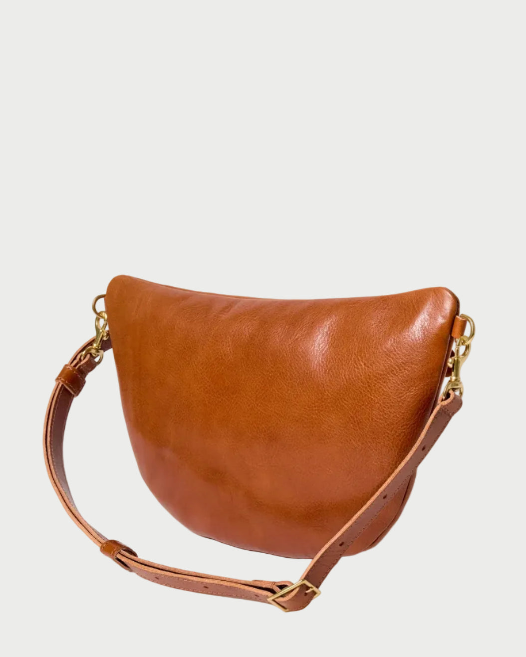 The CLARE V. Clare V. Old Fashion Grande Fanny is a brown crossbody bag crafted from vegetable-tanned Italian leather, featuring a curved shape, adjustable strap, and gold-tone hardware, displayed against a plain white background.