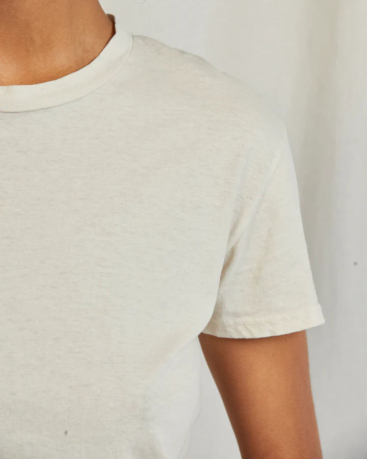 A close-up of a person wearing the Bright Ivory Harley T-Shirt by perfectwhitetee against a neutral background, focusing on the neck, shoulder, and upper arm. The face is not shown; styled simply with mid-rise denim.