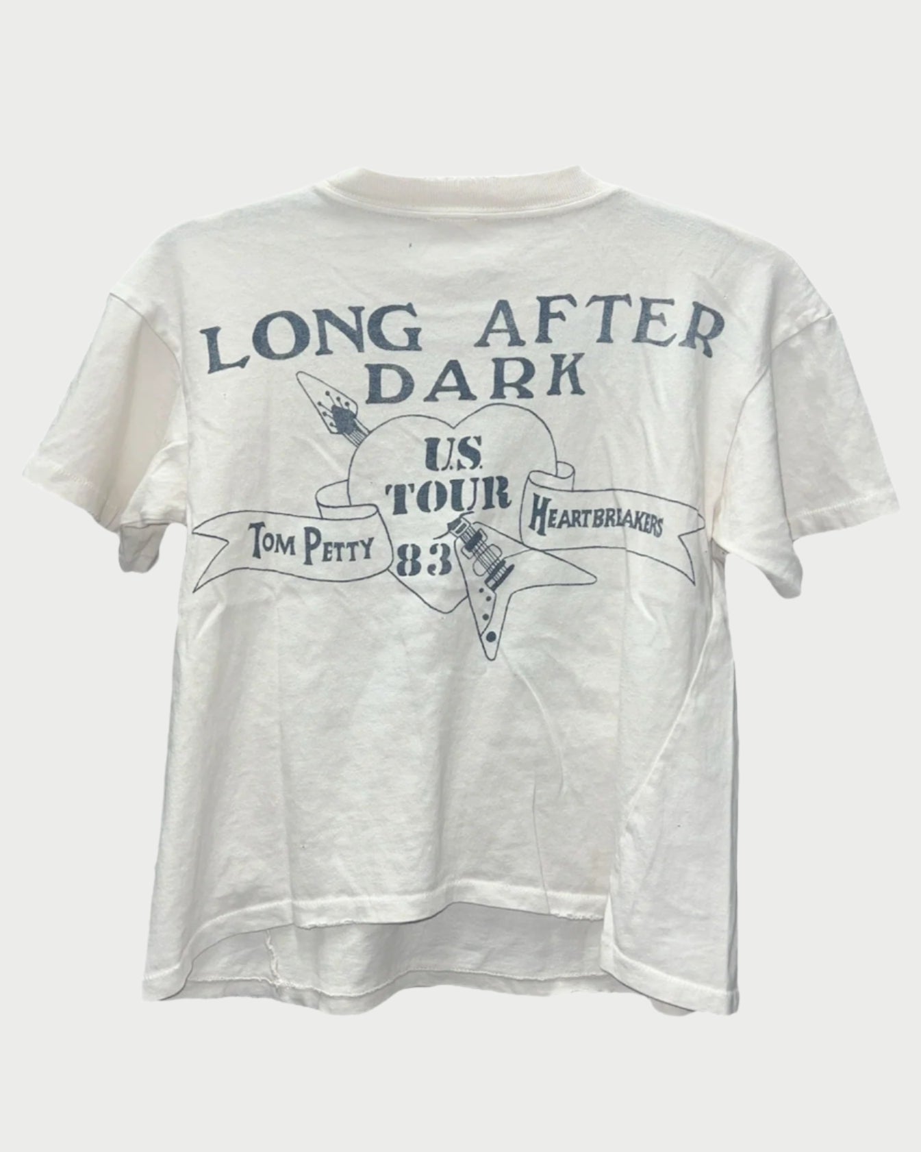 Explore the Madeworn Tom Petty Tee, crafted from 100% white cotton with a vintage fit. It showcases the "Long After Dark" US Tour '83 design, featuring an electric guitar graphic and a banner with "Tom Petty" and "Heartbreakers.