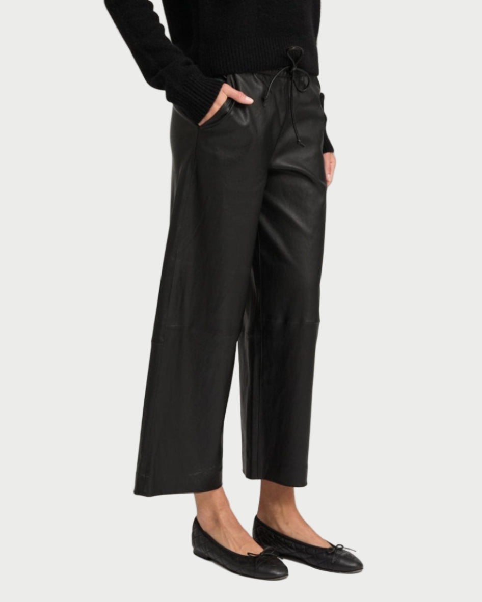 Wearing SPRWMN Cropped Leather Baggy Pants with a drawstring waist, a black sweater, and black ballet flats, a person stands with hands in pockets against a plain background.