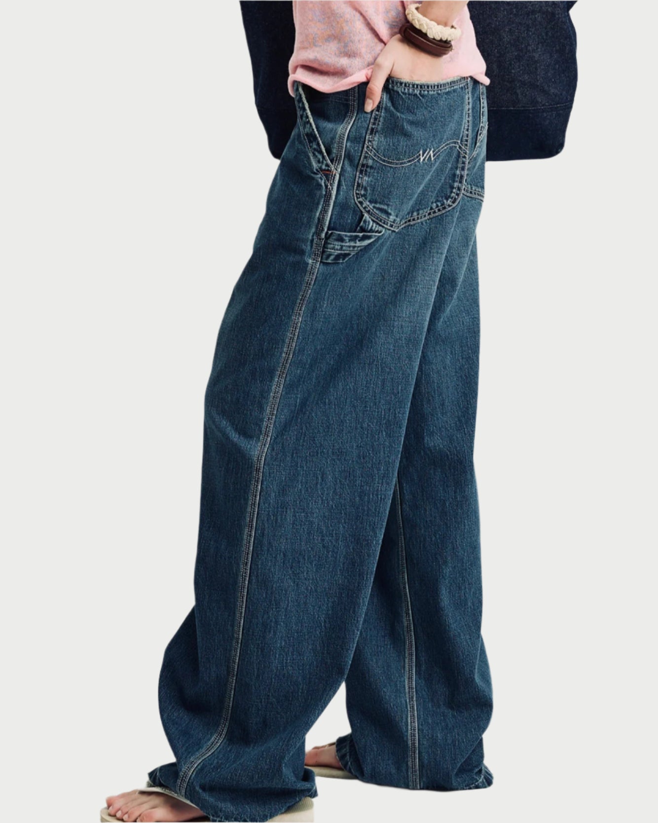A person stands barefoot against a white background, wearing the Denimist Teri Wide Leg Carpenter Pant in 100% cotton denim and a light pink shirt, with one hand in their pocket.