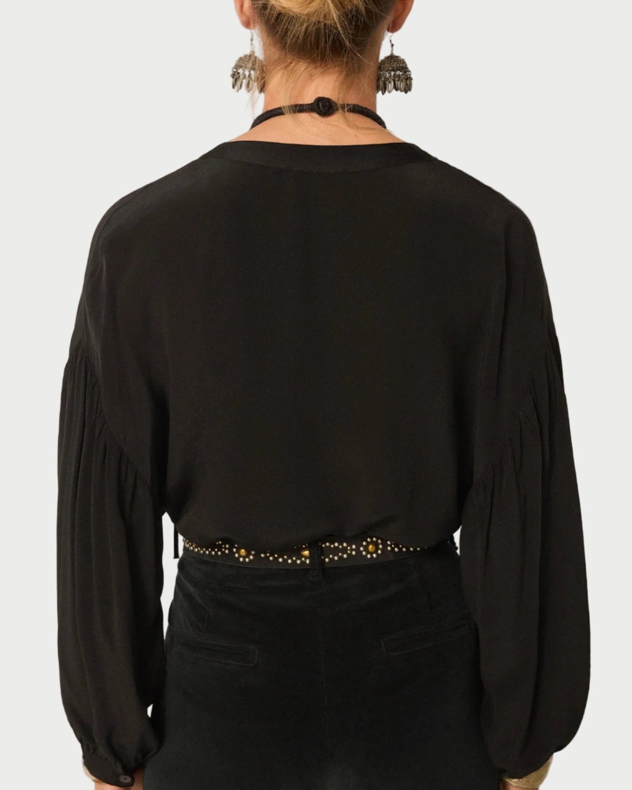Person wearing a black blouse with long sleeves and a belt against a plain background