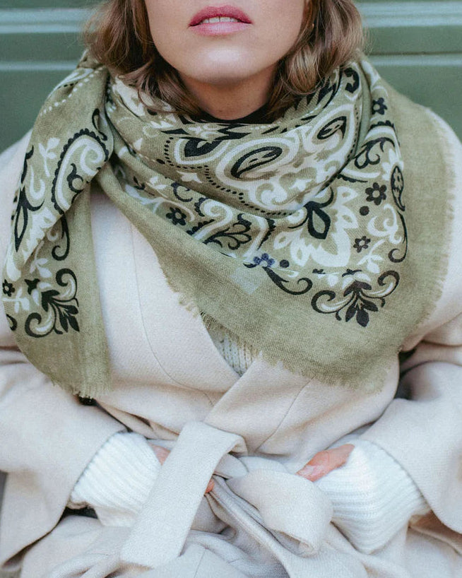 Person wearing a patterned scarf and cap against a green background
