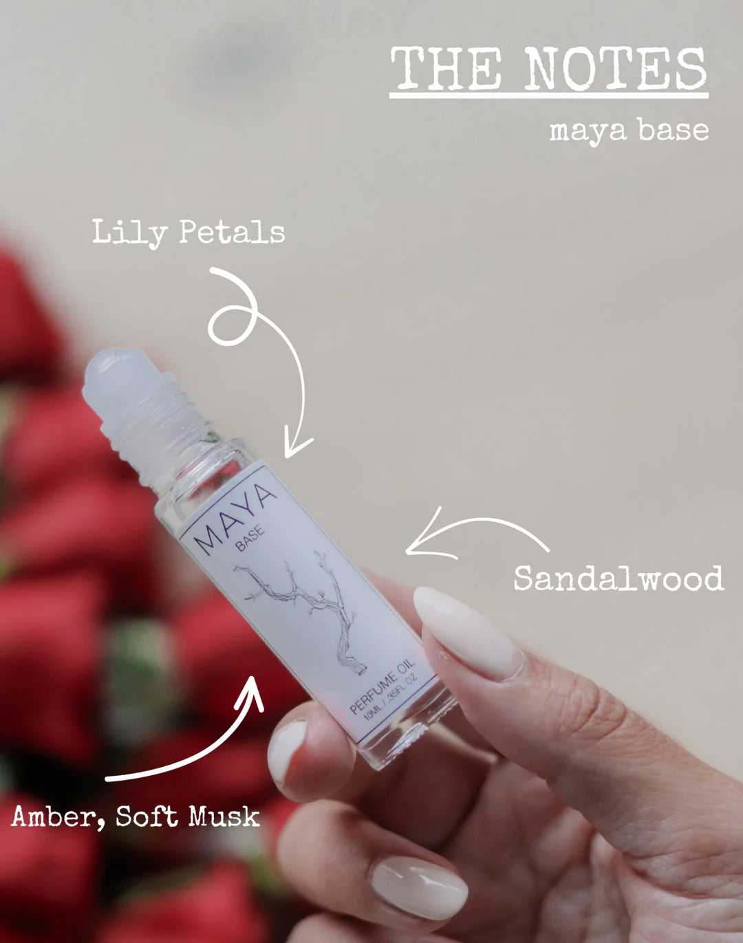A hand holds a clear 10ML MAYA Base Perfume Oil rollerball. Text highlights notes of lily petals, sandalwood, amber, and soft musk. Red flowers are blurred in the background.