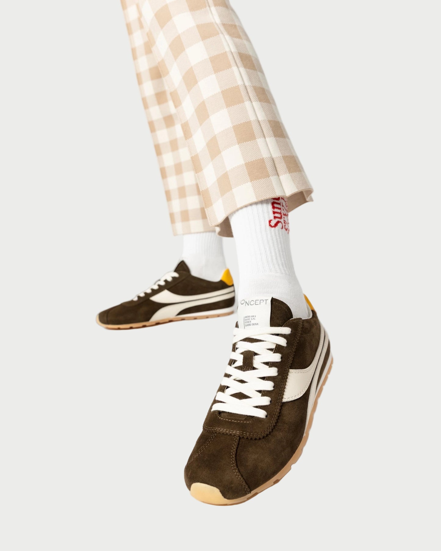 Brown sneakers with white laces worn with plaid pants and white socks on a white background