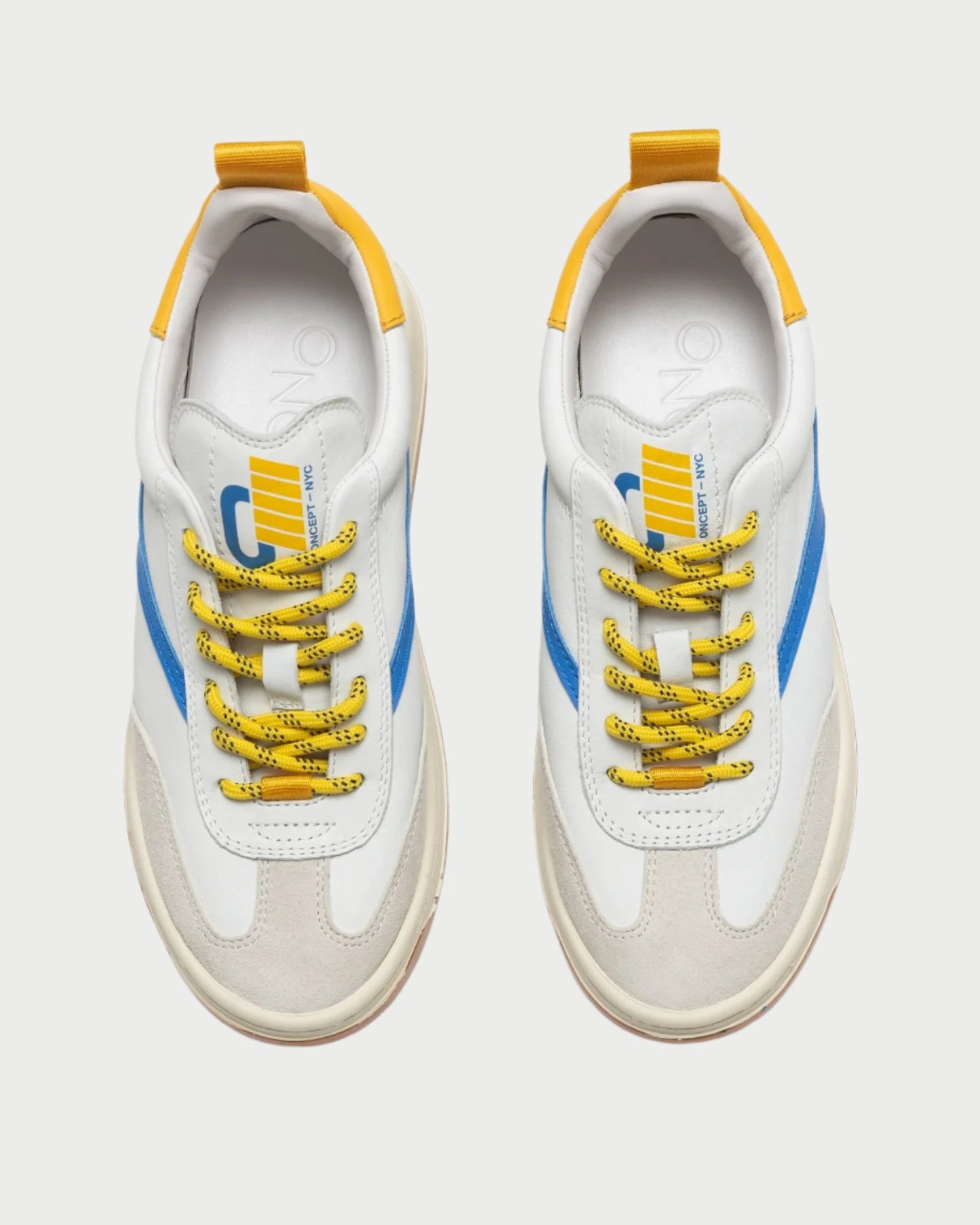 Bird's-eye view of a pair of fashionable Oncept Panama Sneakers showcasing white uppers, blue side stripes, yellow accents, and yellow speckled laces. The insoles feature a branded logo design. These comfortable sneakers offer a contemporary sporty appearance ideal for any casual occasion.