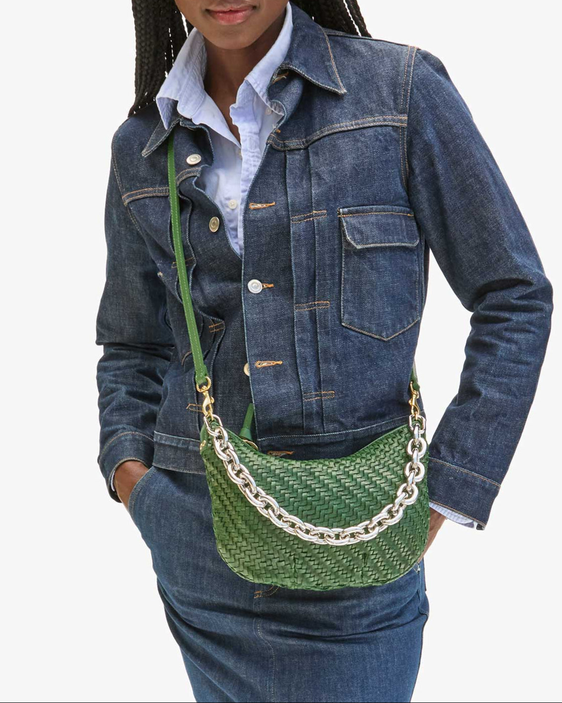 Woman wearing a denim jacket with a green handbag on a white background