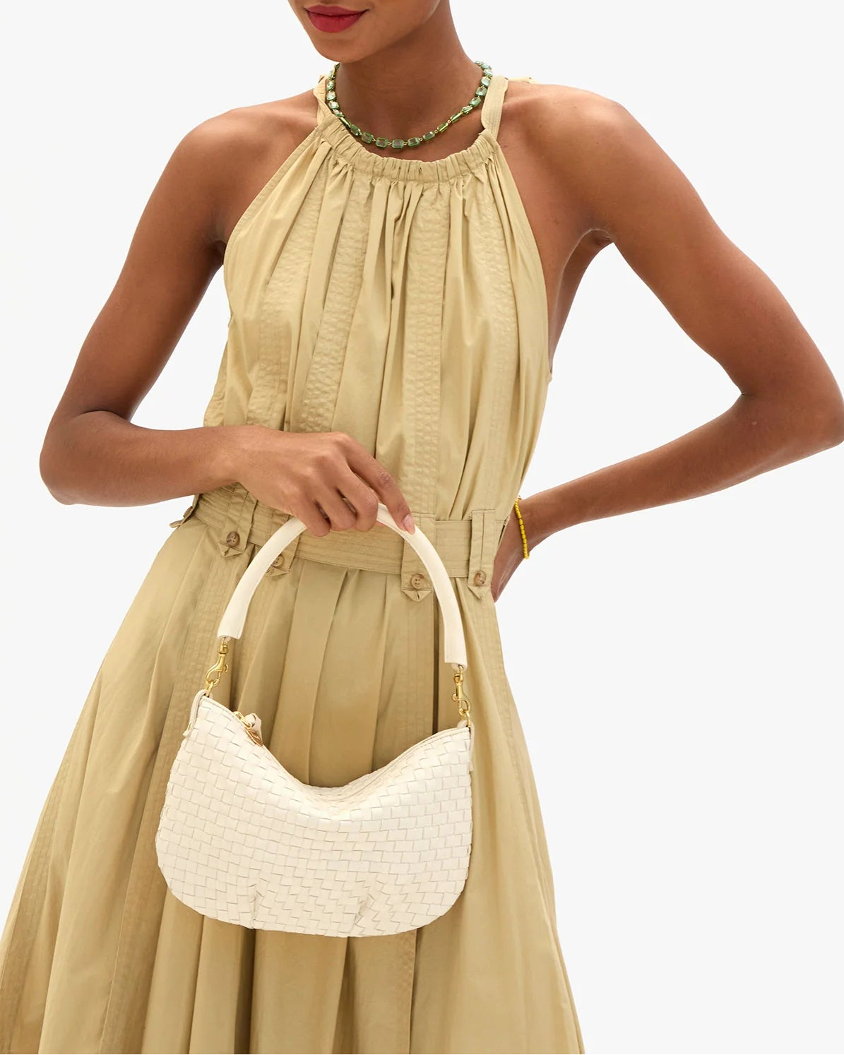 Woman in a beige dress holding a white handbag against a white background