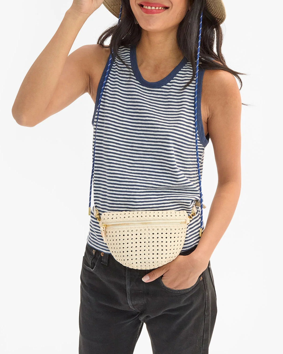 Woman wearing a striped tank top, black pants, and a straw hat with a beige woven belt bag.